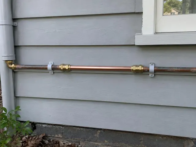 Repaired copper water pipe on grey weatherboard wall beside a window in Paddington