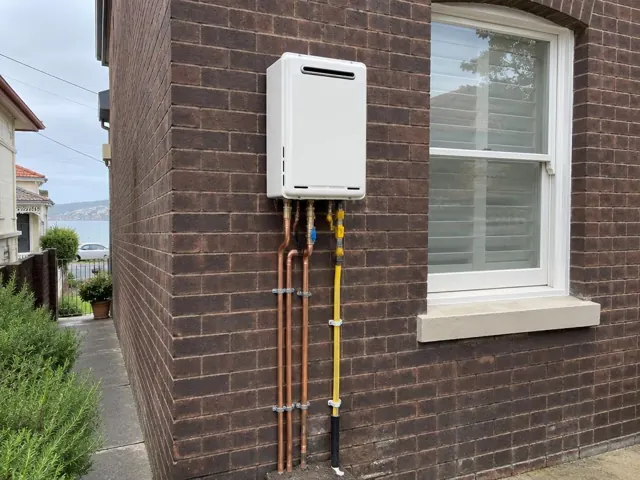 Wall-mounted hot water unit on a brick exterior wall beside a window in Bondi