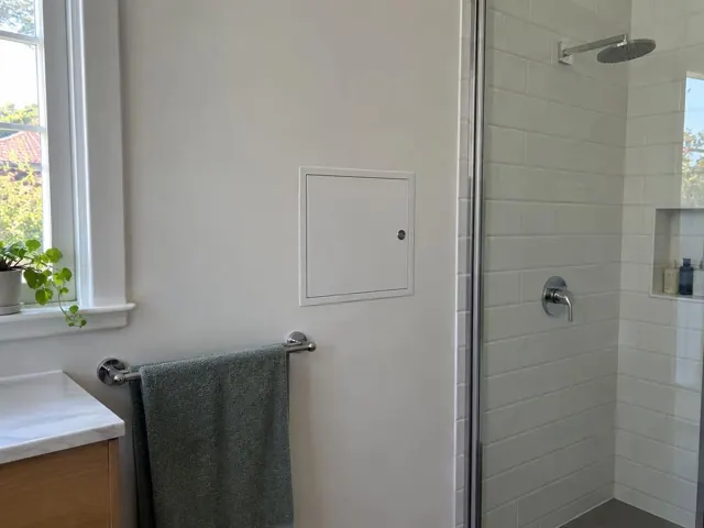 Small access panel in a painted bathroom wall beside a towel rail and shower in Bellevue Hill